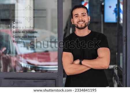 Half-length portrait of a barber leaning with his arms crossed on the door of his barber shop. The letters says in Spanish the words cut, shaved, beard and retired. Royalty-Free Stock Photo #2334841195