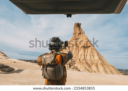 Rear View Of A Man With A Hat Taking A Photo With A Smart Phone From His Van In The Bardenas Desert. Navarre