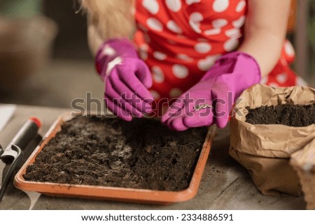 Woman planting flowers in the soil and watering it. Cropped view of a girl in white dress working with flowerpot in the greenhouse