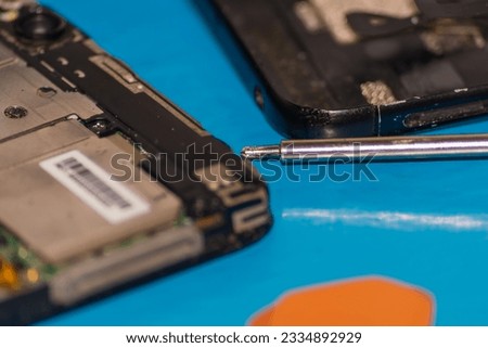 A disassembled smartphone inside which a lot of dirt has accumulated. The concept of precision work on the repair and maintenance of computer and mobile equipment. Manual mini screwdrivers