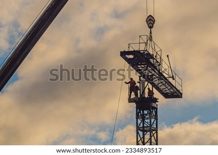 A construction worker rigging with a crane hook at a height against a partially cloudy sky with some out of focus. One of the dangerous work of the world. Fall protection guards installed. Royalty-Free Stock Photo #2334893517