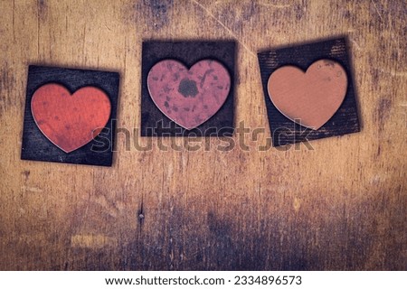 Three dirty inked stained vintage letterpress hearts on a aged wooden background.