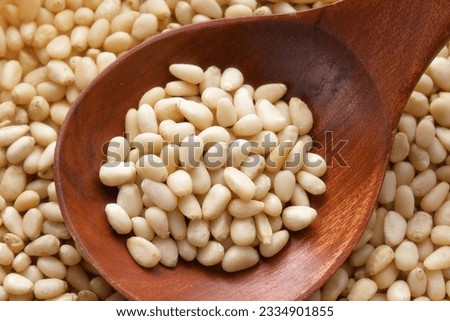Cleaned pine nuts. Pine nut kernels lie in wooden spoon. Top view of nuts close-up. Advertising photography for marketplaces or online stores.