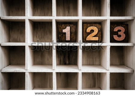 The numbers -123- written in vintage ink stained wooden letterpress type in a partitioned printer-s drawer.