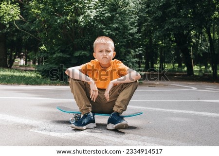 Outdoor activities for children.A cheerful young boy in bright clothes sits on a skateboard. Caucasian schoolboy on a walk. Front view