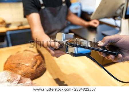 A customer pays for a loaf of bread and muffins using a mobile phone at the bakery's checkout counter.