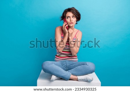Full length photo of minded doubtful person sit podium finger touch chin speak telephone isolated on blue color background