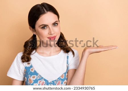 Portrait of satisfied nice woman ponytails hairdo dressed white shirt arm presenting offer empty space isolated on beige color background