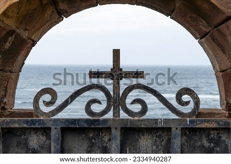 Mysterious graveyard metal gate with cross and sea skyline background