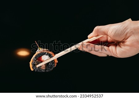 Tuna Dragon roll in chinese chopsticks in hand on the blurred background