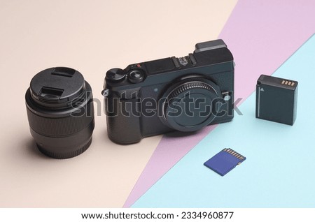 Photographer's equipment. Modern digital mirrorless camera with lens, battery and sd memory card on pastel background.