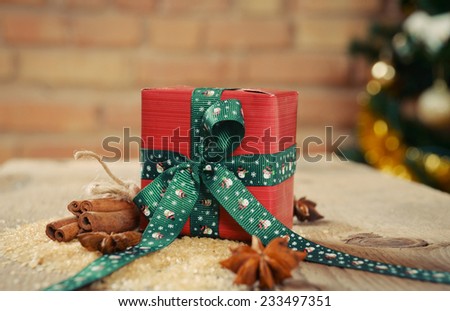 small gift with cinnamon for Christmas on old wooden table and re brick background, holiday concept