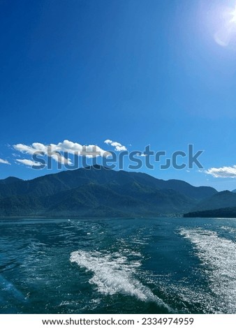 Blue Sun Moon Lake in Taiwan with tall mountains in the background, under a clear sky with a few clouds on a sunny summer day.