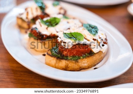 Tasty bruschetta with green pesto, red tomatos and white burrata creamy cheese. Delicious appetizer plate in Italian restaurant. Royalty-Free Stock Photo #2334976891