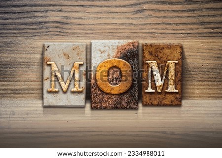 The word -MOM- written in rusty metal letterpress type sitting on a wooden ledge background.