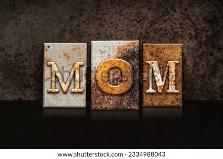 The word -MOM- written in rusty metal letterpress type on a dark textured grunge background.