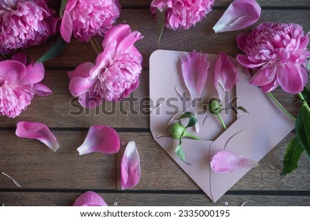 Cup of coffee and pink peonies on a wooden background. Top view, copy space.