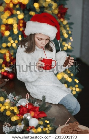 Girl in Santa hat for Christmas eats cookies and cocoa at home in kitchen