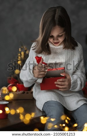 Merry Christmas and Happy New Year 2023. Happy girl opens gift on background of lights