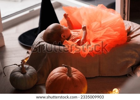 beautiful baby girl in witch halloween costume at home, lying on bed with Halloween decoration, pumpkins 
 and orange skirt, Lifestyle indoors Royalty-Free Stock Photo #2335009903
