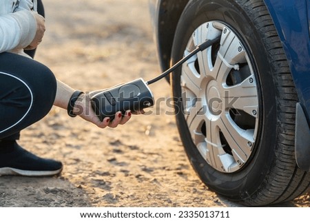 A woman's hand holds a wireless portable air pump for inflating car tires. Royalty-Free Stock Photo #2335013711