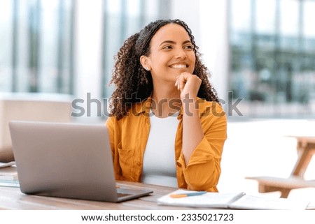 Positive brazilian or hispanic curly haired girl, freelancer, female student, IT specialist, sit outdoors, with laptop, looks happily to the side, thinking about something good, dreaming, smiling