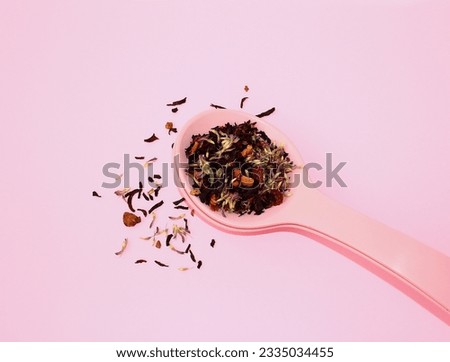 Dried tea leaves with fruits and flowers in a large spoon on a pink background. The concept of fragrant healthy tea. Top view.