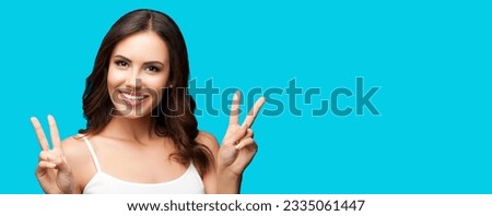 Photo of woman showing two fingers or victory hand sign gesture, over aqua blue green studio background. Happy smiling gesturing brunette girl. Wide banner composition with mock up copy space.