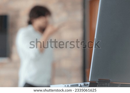 A laptop on a desk and an unrecognizable businessman sending a voice note out of focus in the background. homeoffice. Communication and technology concept.