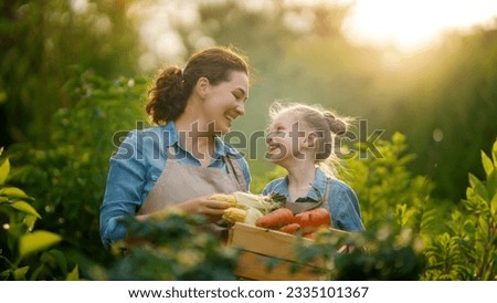 Happy mother and daughter gardening in the backyard organic garden. Kid and mom picking fresh vegetables and learning botany.  Royalty-Free Stock Photo #2335101367