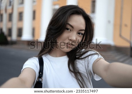 Attractive asian brunette woman wearing white t-shirt and making selfie on the street