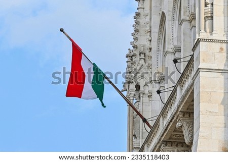 Hungarian flag on a flagpole hanging on the facade of the Hungarian Parliament building