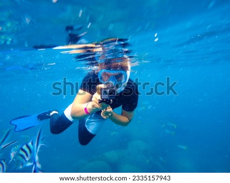 A caucasian man takes pictures on an underwater camera while snorkeling on a tropical reef
