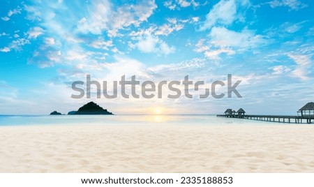 A pier on a beach, with the sun setting in the background