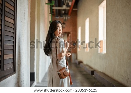 Back view of a beautiful Asian female tourist in a minimal dress is walking along the building, and enjoying strolling around the city.