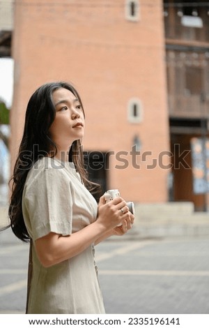 A portrait of a beautiful Asian female tourist in casual clothes strolling around the city and shooting cityscapes with her instant camera. Lifestyle concept
