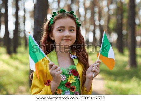 Pretty little girl celebrating St Patricks Day and waving with flags of Ireland dressed as a fairy 