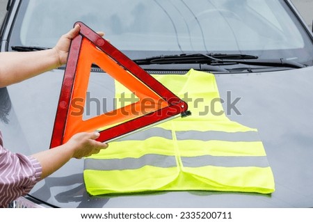 hands holding warning triangle and yellow reflective vest. Safety in case of breakdown on highway