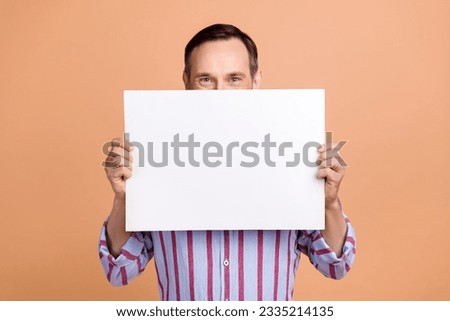 Photo of senior positive person hands hold empty space paper proposition blank cover half face isolated on beige color background