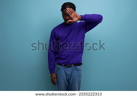 portrait of an emotional dark-skinned african young guy in a blue sweatshirt and jeans in the studio