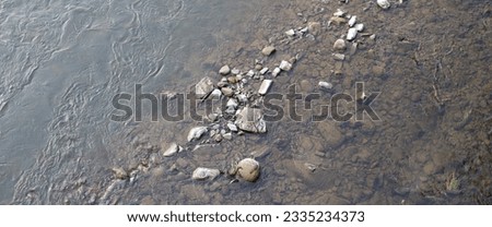 The riverbed is covered in small rocks and pebbles. The water is shallow and clear, and you can see the rocks through the water. Royalty-Free Stock Photo #2335234373