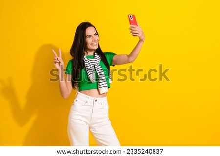 Photo of excited friendly girl dressed green t-shirt recording video gadget showing v-sign empty space isolated yellow color background