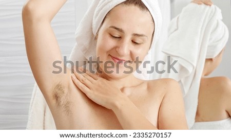 Portrait of smiling natural woman with growing armpit hair posing in bathroom. Concept of hygiene, natural beauty, feminity and body hair growth