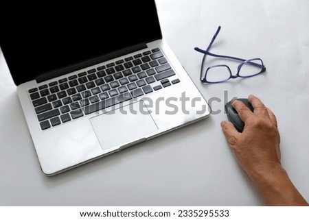 Top view of man's hand operating a computer mouse next to laptop and glasses over white background
