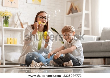 Nanny with little boy blowing soap bubbles at home Royalty-Free Stock Photo #2335299773