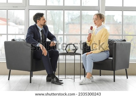 Female journalist with microphone having an interview with man in office Royalty-Free Stock Photo #2335300243