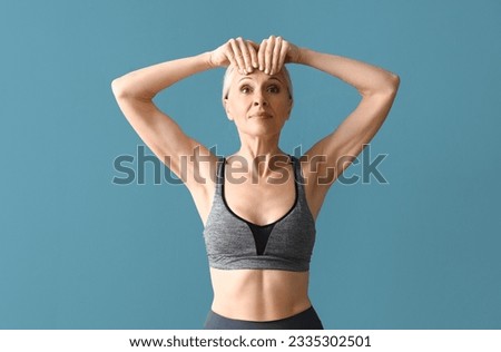 Sporty mature woman doing face building exercise on blue background