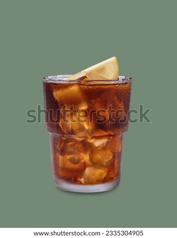 Iced tea, Cuba Libre or Long Island cocktail with cola, lemon and ice in a glass on green isolated background. The concept of a cold refreshing drink or lemonade. Front view and copy space.