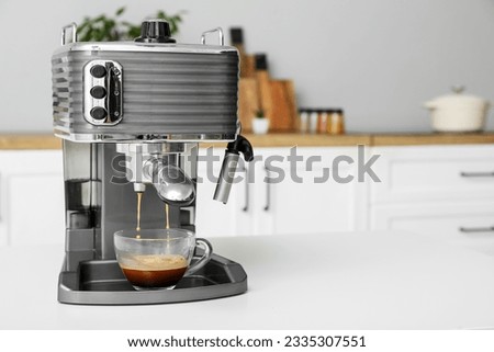 Modern coffee machine with glass cup of hot espresso on table in kitchen Royalty-Free Stock Photo #2335307551