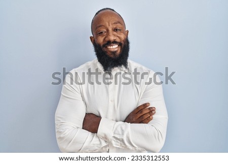 African american man standing over blue background happy face smiling with crossed arms looking at the camera. positive person. 